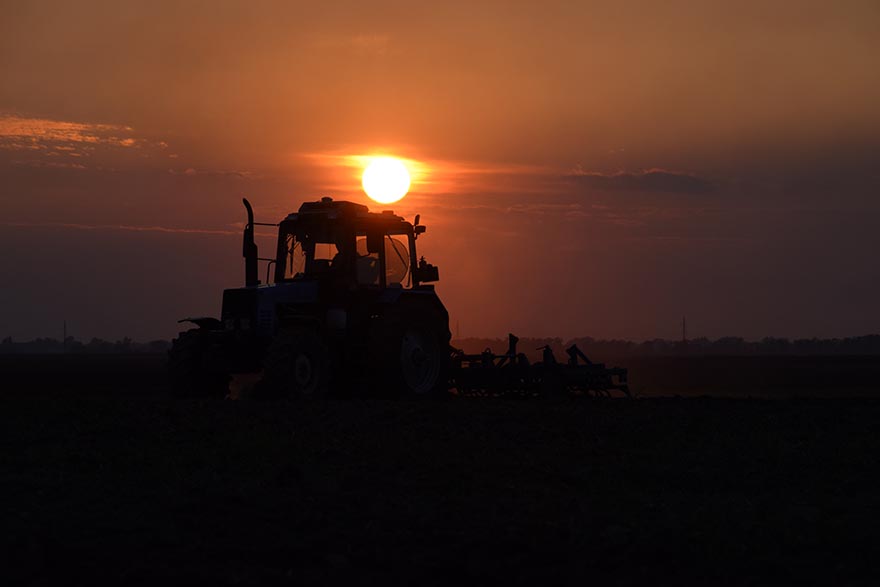 Tractor plowing plow the field on a background sunset. tractor silhouette on sunset background.